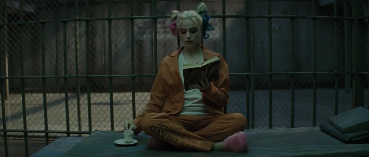 Suicide Squad (2016) movie still: medium — A dimly lit prison enclosure features vertical steel bars and a thin mattress. A woman with blonde…
