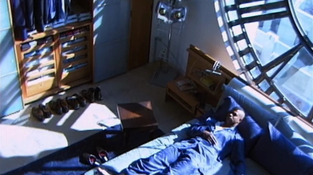 Bamboozled (2000) movie still: wide — A modern bedroom with minimalist wood furniture features a large prominent circular window. A man in blue…