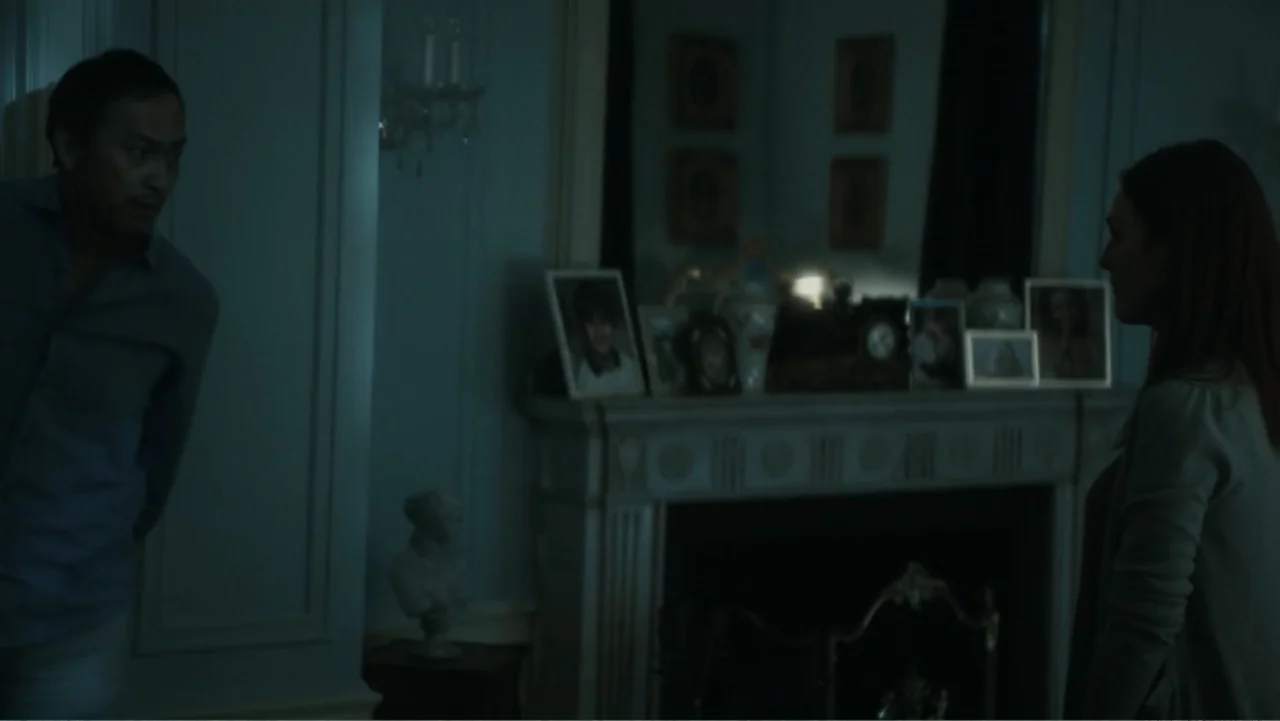 Bel Canto (2018) movie still: medium — An interior space features a classic fireplace mantle decorated with framed photographs and vases. A man and…