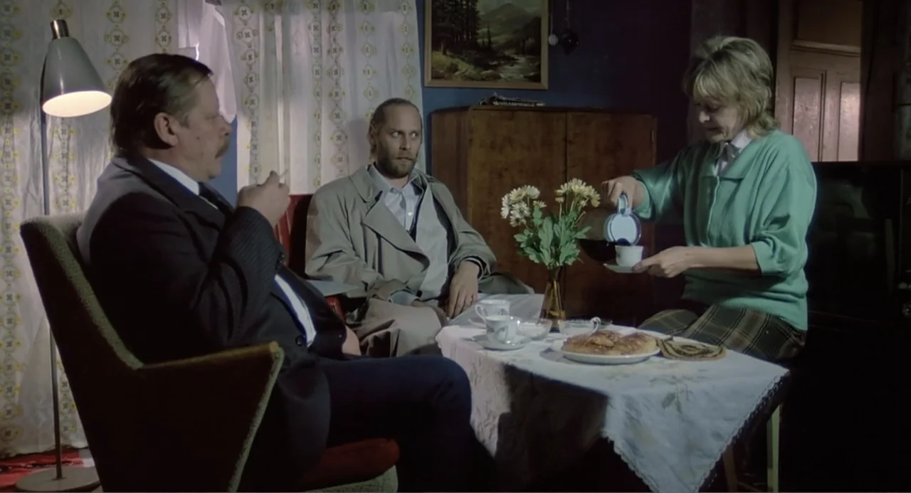 The Match Factory Girl (1990) movie still: medium — A modest living room contains a table set with coffee and baked goods. A woman pours coffee…
