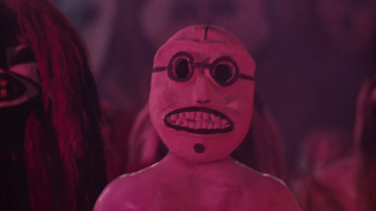 Altered States (1980) movie still: closeup — A dimly lit space filled with magenta light and indistinct background figures. A central subject wears…