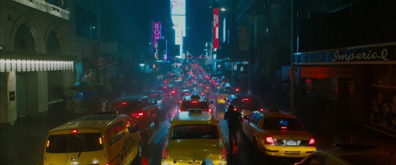 John Wick: Chapter 3 – Parabellum (2019) movie still: wide — A congested urban thoroughfare is filled with yellow taxis and vehicles at night. Rain…