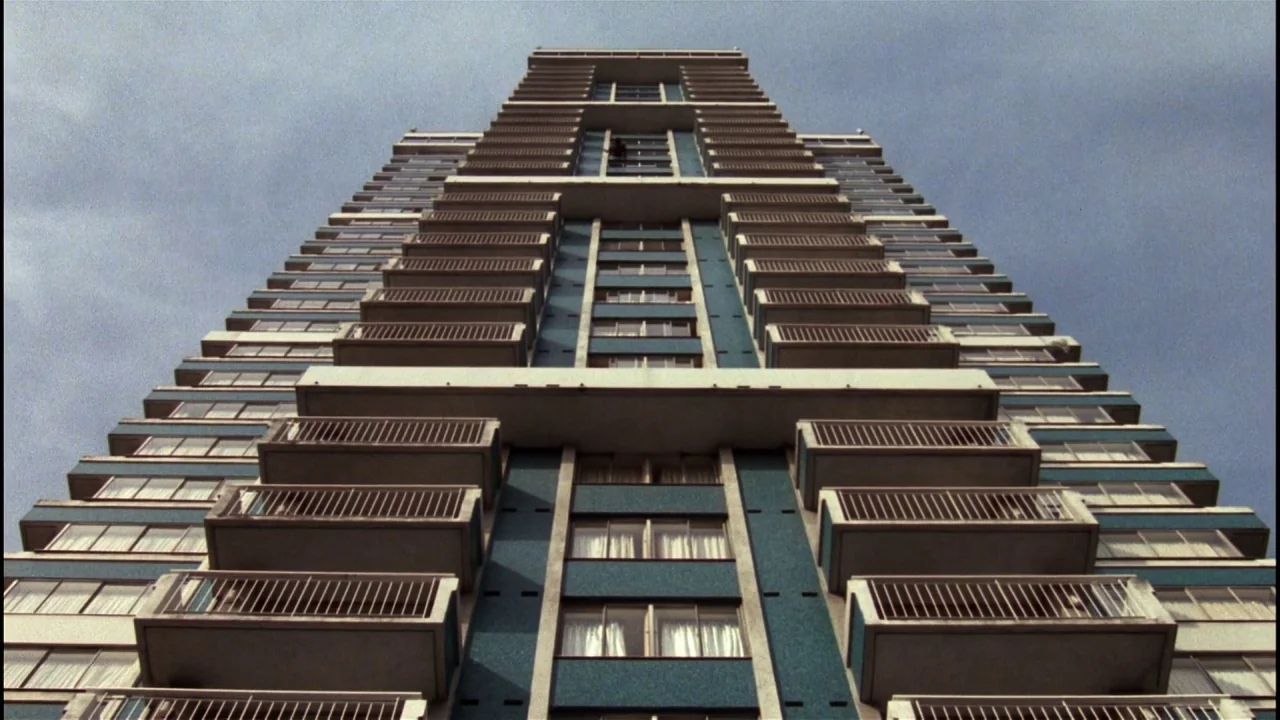 Star 80 (1983) movie still: establishing — A tall mid-century apartment block features repetitive balconies and blue facade accents. The camera…