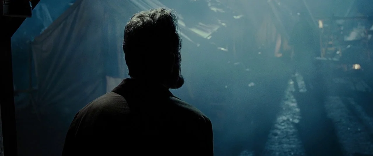 Lincoln (2012) movie still: medium — A hazy military camp filled with dense smoke and rows of canvas tents. A man with a dark coat stands in the…
