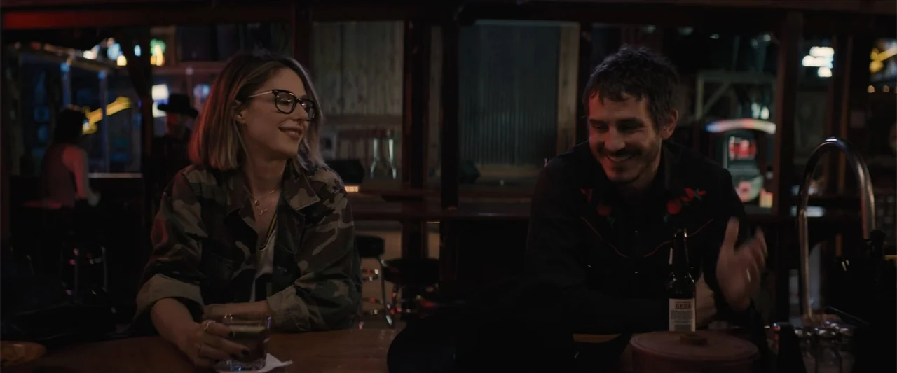 Equation of Love and Tone Deafness (2015) movie still: medium — A dimly lit bar interior features wooden surfaces and dark background shadows. A man…