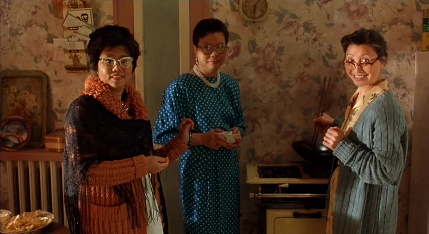 Double Happiness (1994) movie still: medium — A domestic space features floral wallpaper, a wall clock, and a vintage stove. Three women stand…