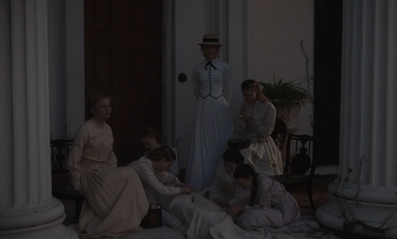 The Beguiled (2017) (2017) movie still: wide — A group of women and girls sit on the porch of a large house. They are engaged in sewing, with white…