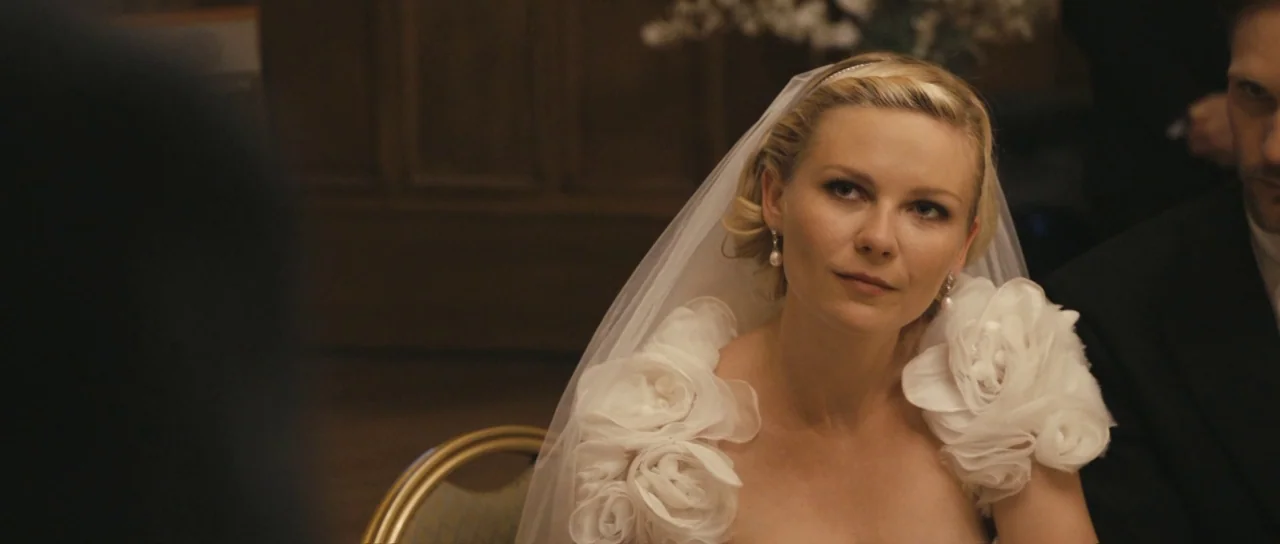 Melancholia (2011) movie still: medium — A banquet hall interior with dark wood wall panels. A bride and a man in a suit sit at a table.