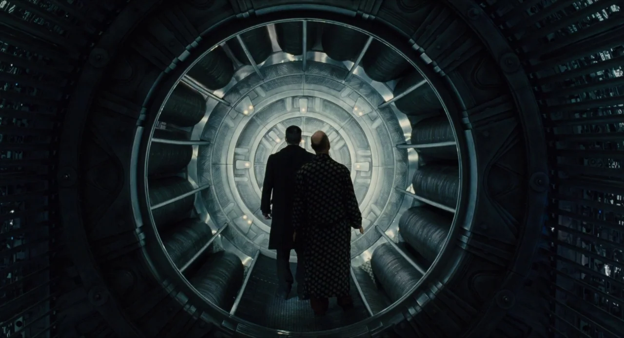 Snowpiercer (2013) movie still: wide — A metallic circular tunnel features concentric rings of cooling fins lining the walls. Two men walk away from…
