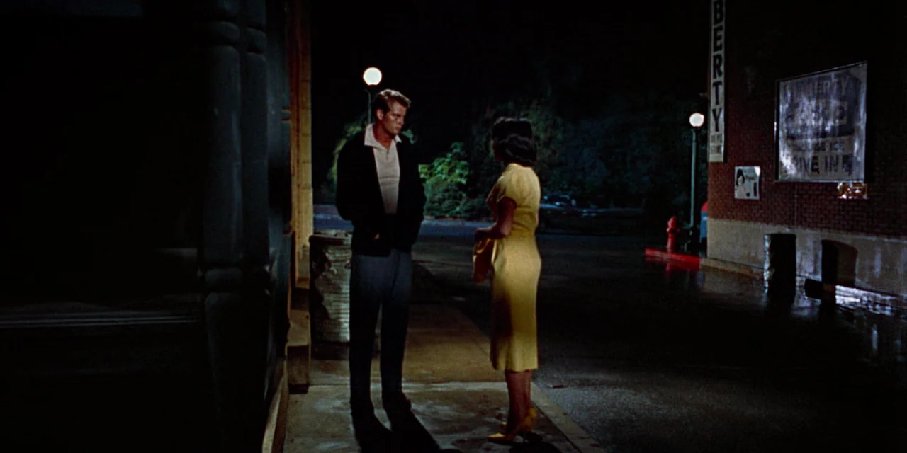 Imitation of Life (1959) movie still: fullbody — A dark, paved area outside a storefront features brick walls and a lit street lamp. A man and a…