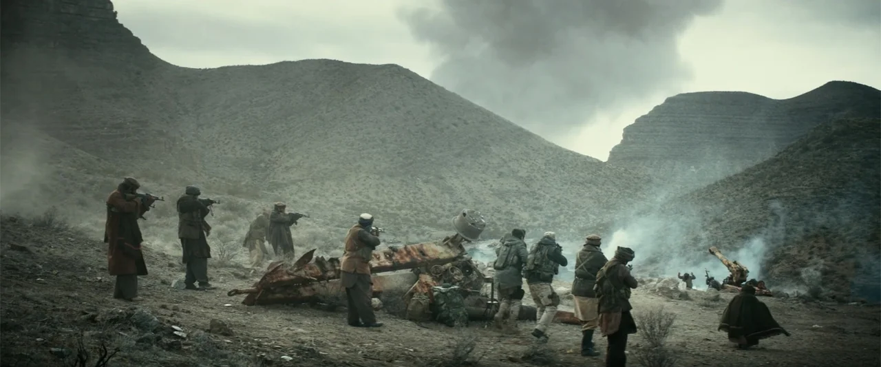 12 Strong (2018) movie still: wide — A group of armed men stand in a barren rocky landscape with sparse vegetation. They aim weapons towards the…