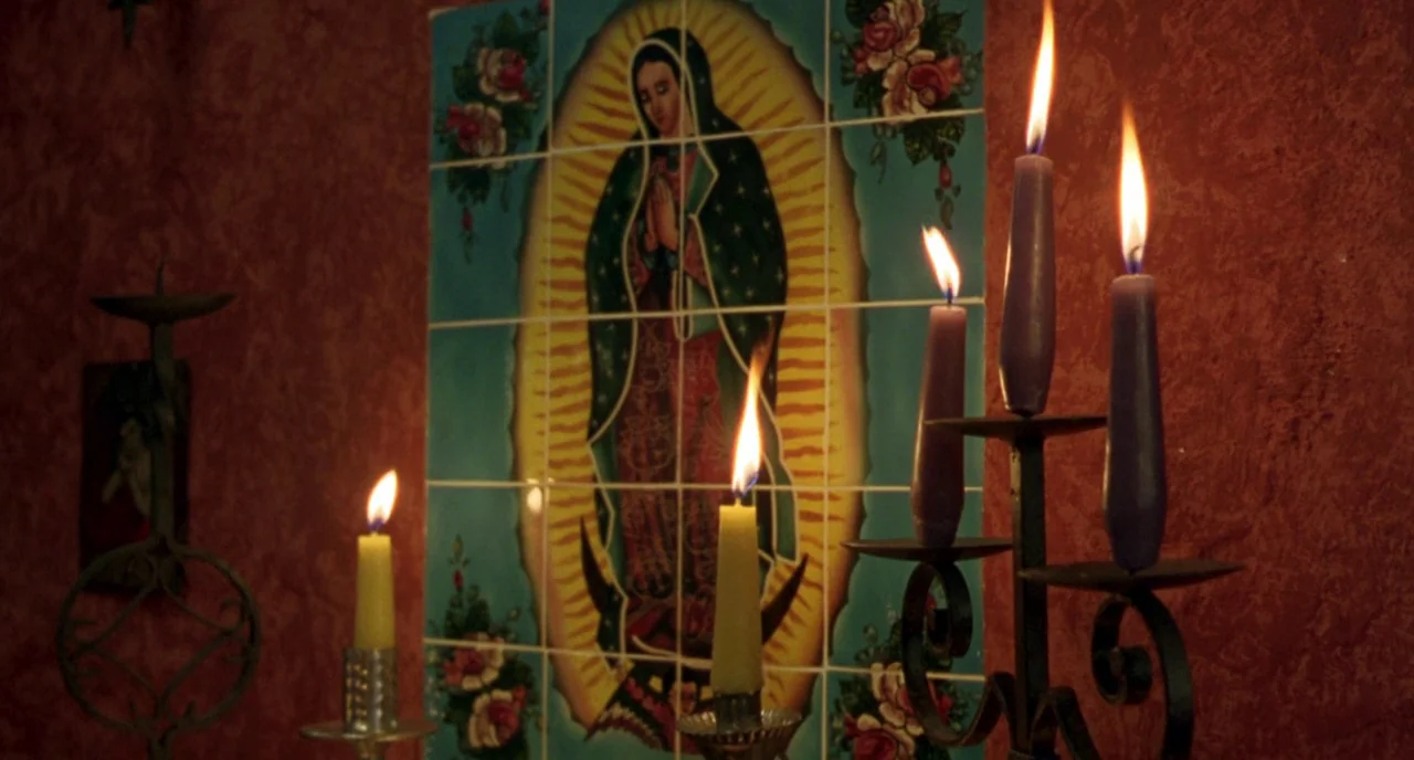 The Craft (1996) movie still: medium — A dimly lit alcove features red textured walls adorned with a religious tile mosaic. Several candles in metal…