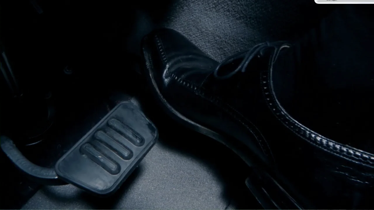 Chain Letter (2010) movie still: closeup — A dark vehicle footwell contains rubberized floor matting and metal pedals. A polished black dress shoe…