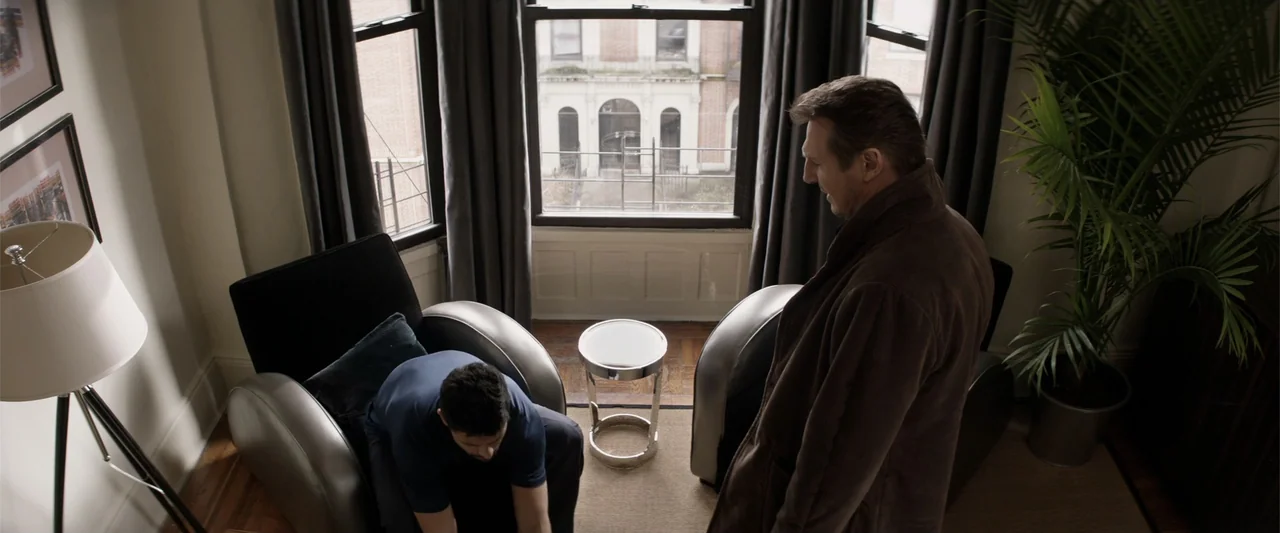 A Walk Among the Tombstones (2014) movie still: medium — An interior apartment room features dark grey curtains, a large window, and modern…