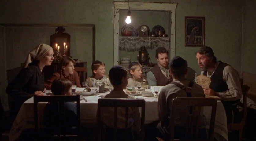 Invincible (2001) movie still: wide — A rustic dining room features green plaster walls and a covered table in center. A family sits together…