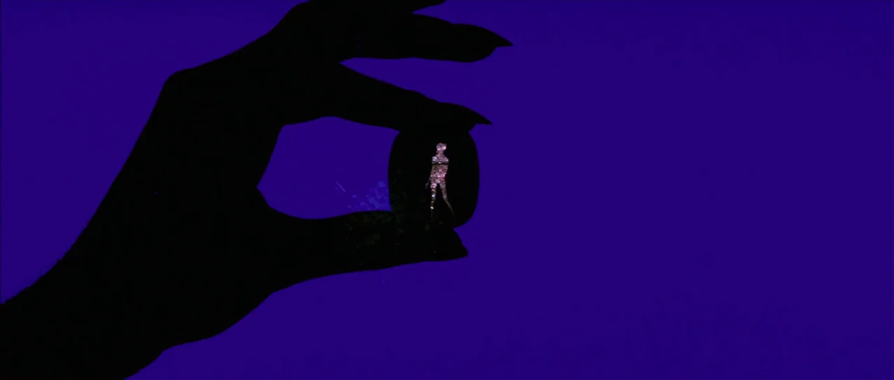 Diamonds Are Forever (1971) movie still: closeup — A silhouette of a large hand holds a small dark stone against a violet background. The stone…