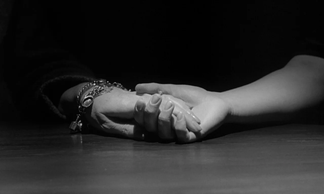 Seance on a Wet Afternoon (1964) movie still: closeup — A wooden tabletop serves as the stage for two hands resting together. One hand wears a charm…