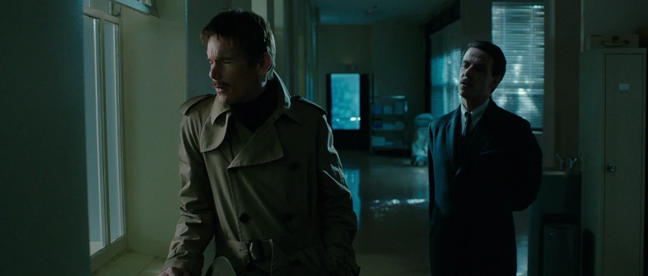 Predestination (2014) movie still: medium — A dimly lit hospital corridor with long fluorescent lights and tiled flooring appears quiet. A man in a…