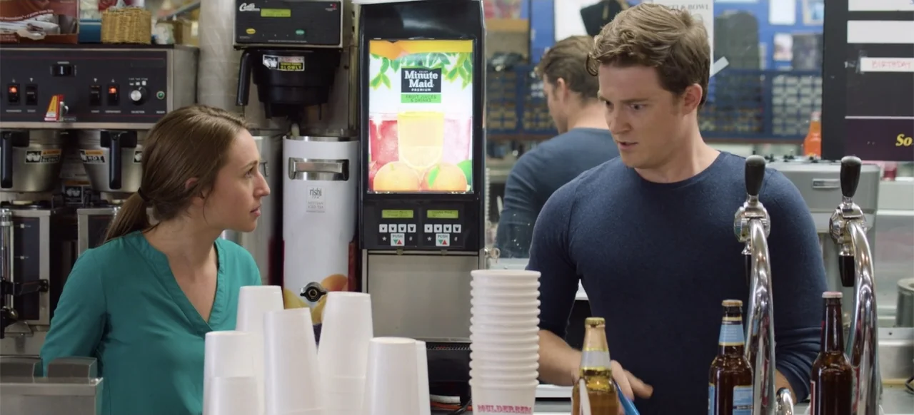Hellbreeder (2004) movie still: medium — A brightly lit concession stand area features beverage dispensers and stacks of paper cups. A woman in…