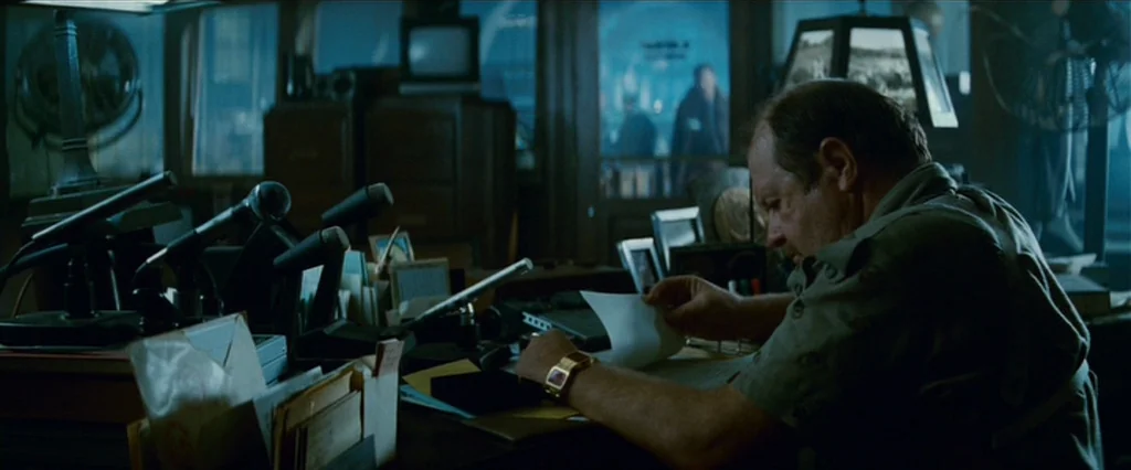 Blade Runner (1982) movie still: medium — A dark, cluttered office space is filled with microphones, stacks of paper, and electronics. An older man…