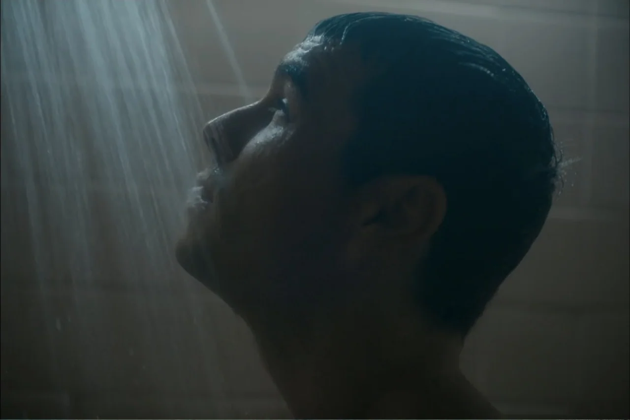 Cross the Line (2020) movie still: closeup — A tiled shower interior with water falling from an overhead fixture. A man with short dark hair is…