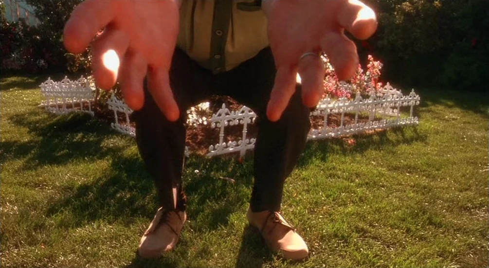 Freddy’s Dead: The Final Nightmare (1991) movie still: closeup — A man stands on a green lawn in front of a small white fence. He holds his hands…