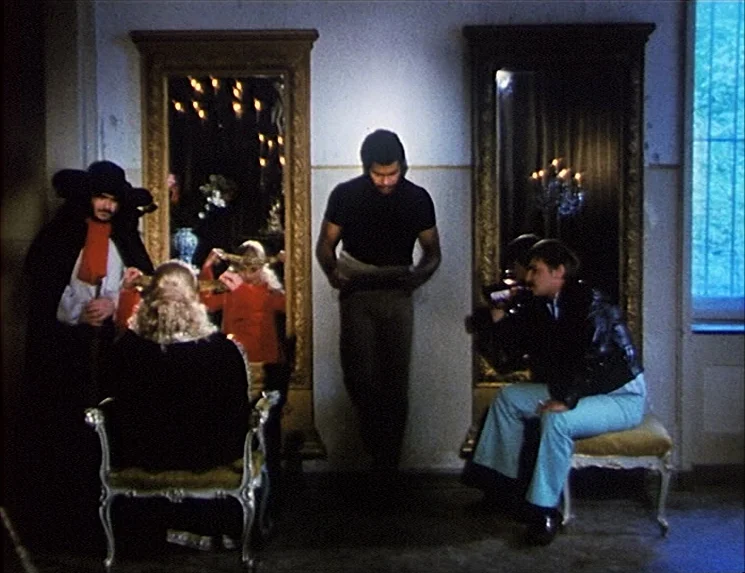 The Niklashausen Journey (1970) movie still: fullbody — A room with two large gold-framed mirrors mounted on a plain white wall. Four people gather…