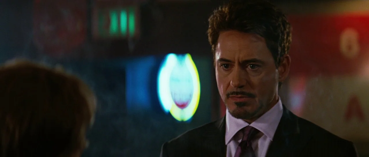 The Incredible Hulk (2008) movie still: medium — A dimly lit room with out-of-focus neon signage and an exit sign visible. A man in a suit looks…