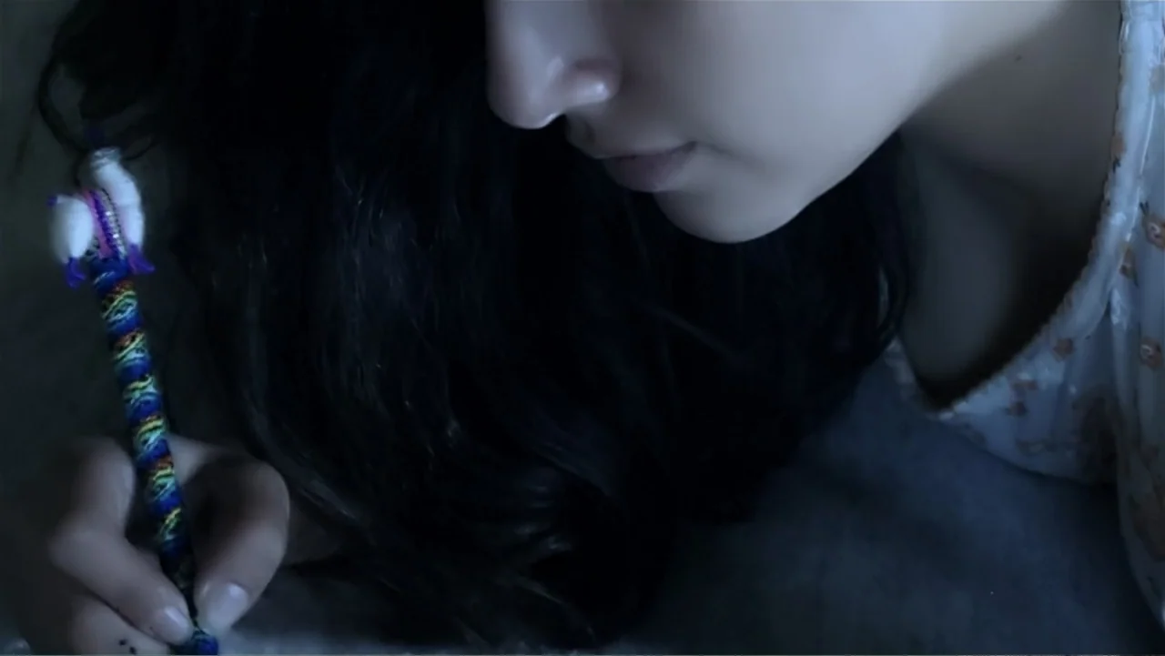 El Duende Sátiro (2016) movie still: closeup — A dimly lit room at night features a person lying down on a surface. A woman in a patterned shirt…