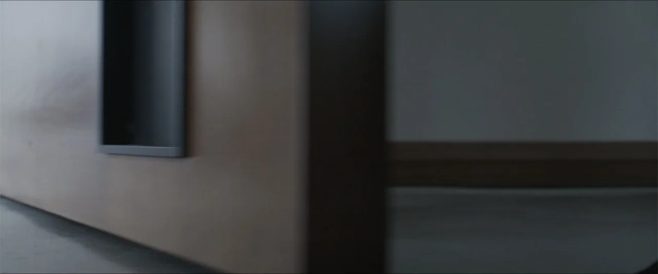 Los habitantes (2023) movie still: establishing — A dark corner of a room features a smooth panel against a plain wall. The composition focuses on…