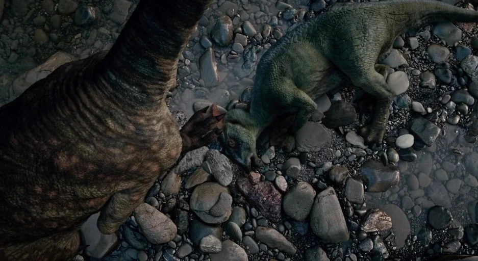 The Tree Of Life (2011) movie still: wide — A wet rocky riverbank contains smooth stones and small pools of shallow water. A large dinosaur and a…