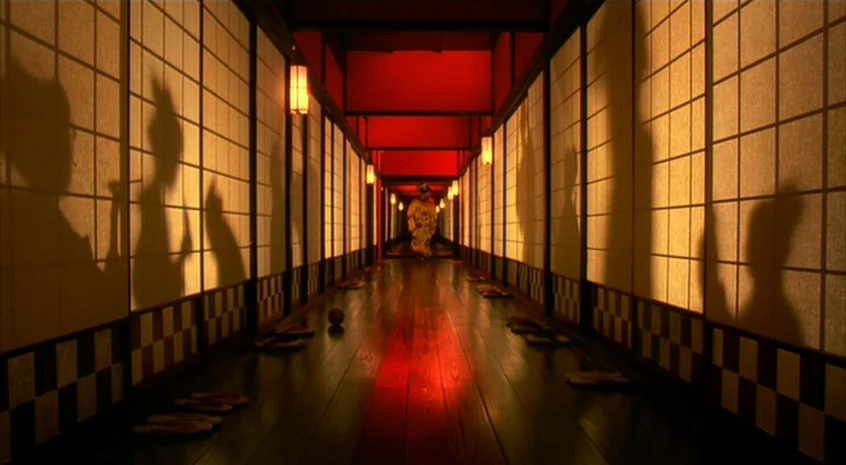 Sakuran (2006) movie still: wide — A long symmetrical wooden hallway is lined with shoji screens on both sides. A lone figure in a traditional…