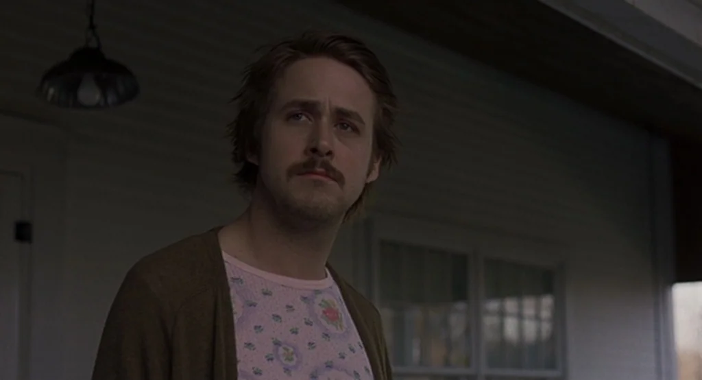 Lars And The Real Girl (2007) movie still: medium — A man stands on a covered porch with white siding behind him. He looks toward the left of the…