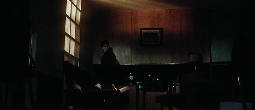 Jigoku (1960) movie still: wide — A dimly lit room features wood-paneled walls and a large, grid-patterned window frame. A man stands in the shadows…