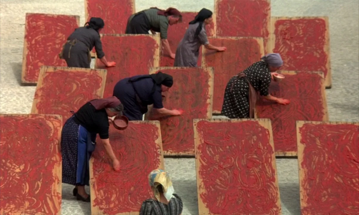 Cinema Paradiso (1988) movie still: wide — A group of women in headscarves work outdoors on a stone-paved plaza. They spread red tomato paste onto…