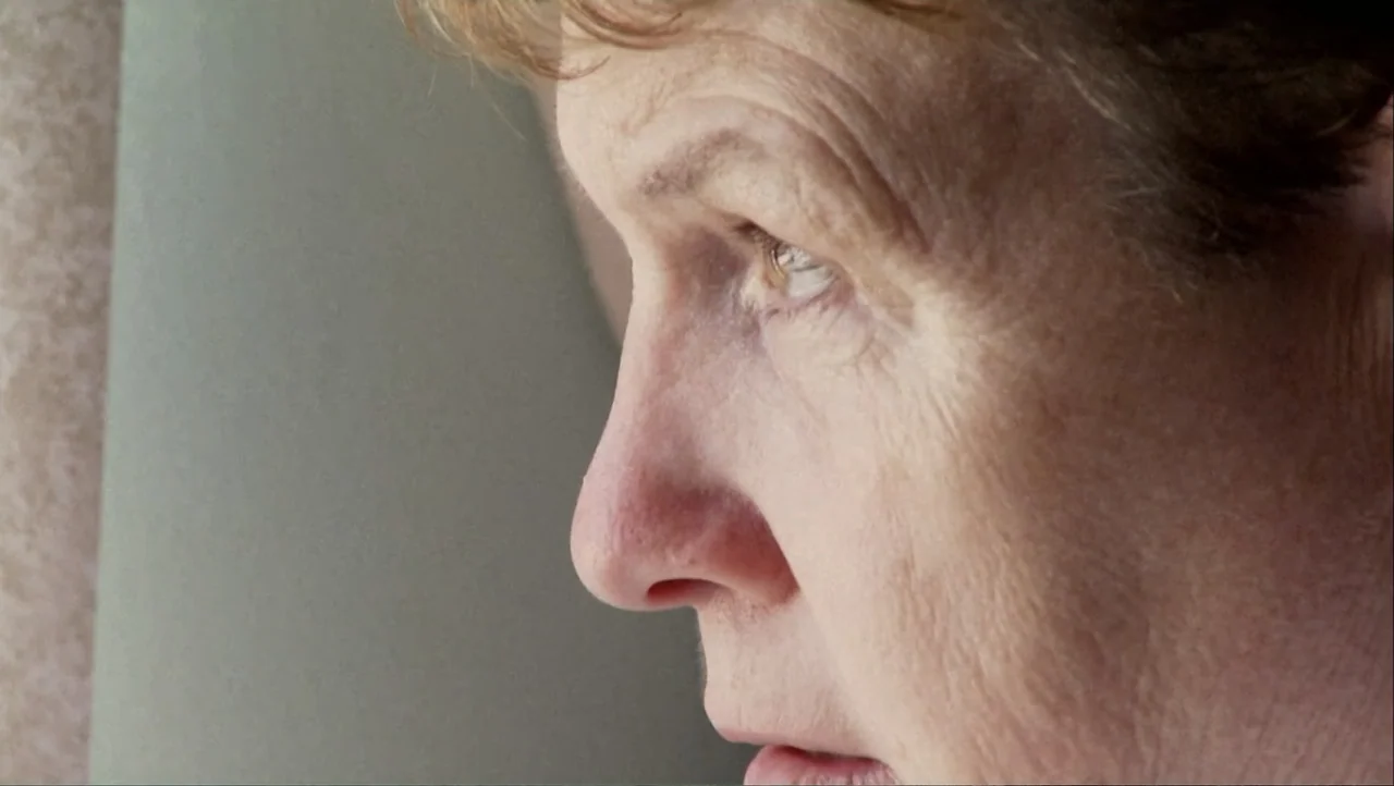 12th & Delaware (2010) movie still: closeup — An interior space with a neutral-colored wall serves as a backdrop. An older woman in profile looks…