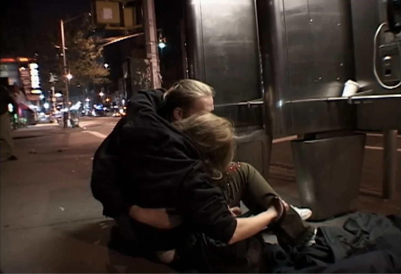 Dope Sick Love (2005) movie still: medium — A night city sidewalk features a metallic public telephone booth and distant street lights. Two people…