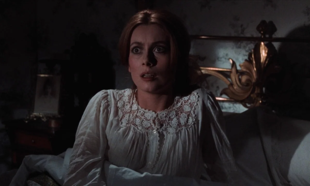 Tristana (1970) movie still: medium — A dimly lit room with ornate wallpaper and a polished brass headboard in view. A young woman sits upright in…