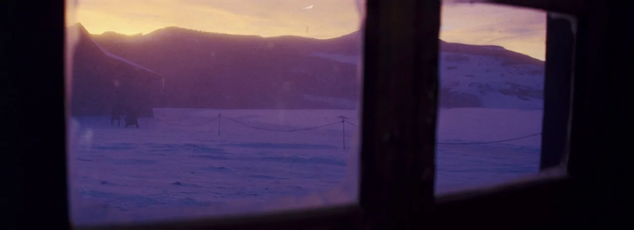 The Hateful Eight (2015) movie still: wide — A view through a wooden window frame looks out over a snow-covered landscape. Distant mountains are…