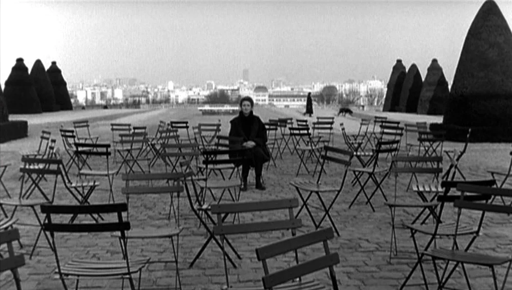 The Tango Lesson (1997) movie still: wide — A wide outdoor terrace features a symmetrical grid of numerous empty metal folding chairs. A woman sits…