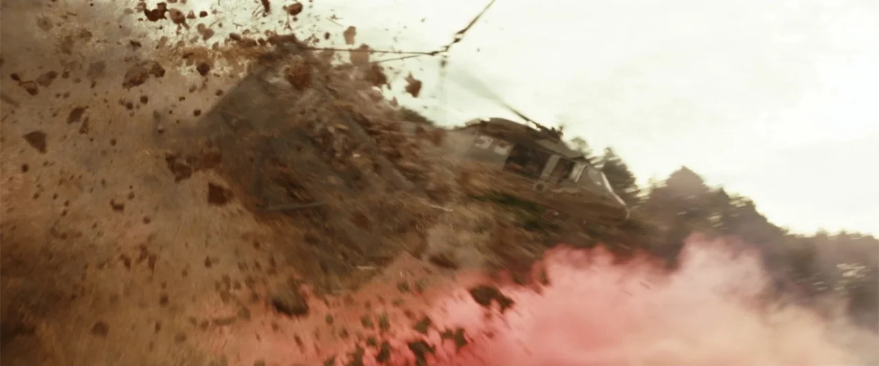 The Tomorrow War (2021) movie still: wide — A military helicopter flies at low altitude above a dusty, rugged outdoor terrain. Debris and dirt…