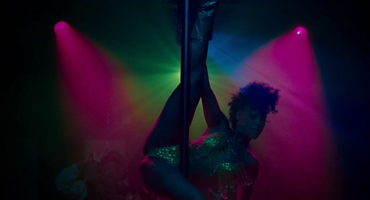 Pariah (2011) movie still: medium — A dark, smoke-filled nightclub space features a vertical pole for dancing. A woman in a gold sequined outfit…