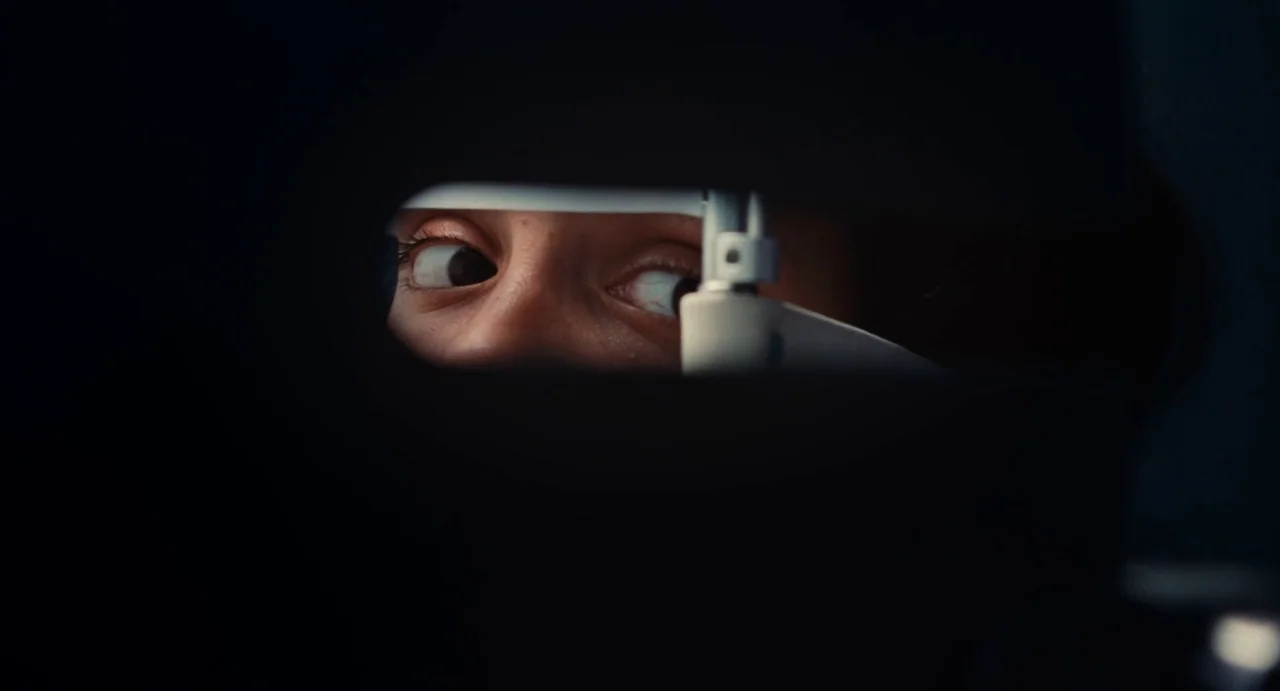 Ava (2017) movie still: closeup — An eye examination device sits in a dark room against a black backdrop. A person looks through the mechanical lens…