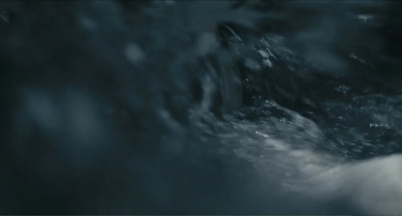 Cowboys (2014) movie still: closeup — Fast flowing water moves over dark stones in a natural outdoor stream. Light catches the white foam of the…