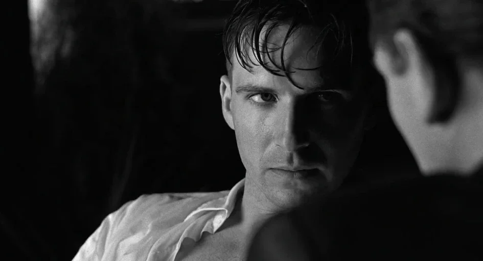 Schindler's List (1993) movie still: closeup — A dimly lit interior space features high contrast lighting and sharp black shadows. A man with damp…