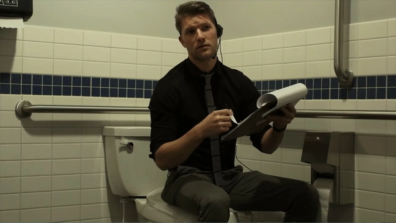 Hello I Love You (2018) movie still: medium — A public restroom with white subway tiles and a blue decorative border stripe. A man in a dress shirt…