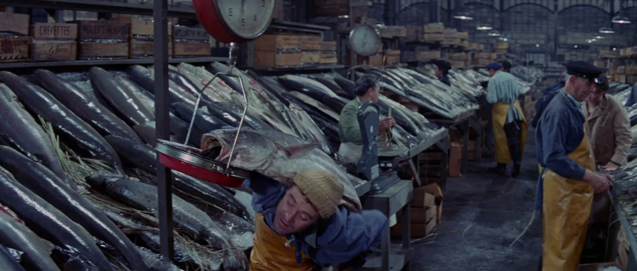 Irma La Douce (1963) movie still: medium — A bustling indoor wholesale fish market features long rows of ice-covered tables. A worker navigates the…
