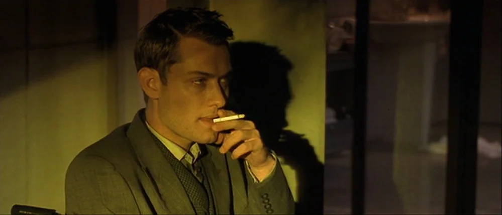 Gattaca (1997) movie still: medium — An interior space features a man sitting in shadow within a yellow-tinted environment. A man with short dark…