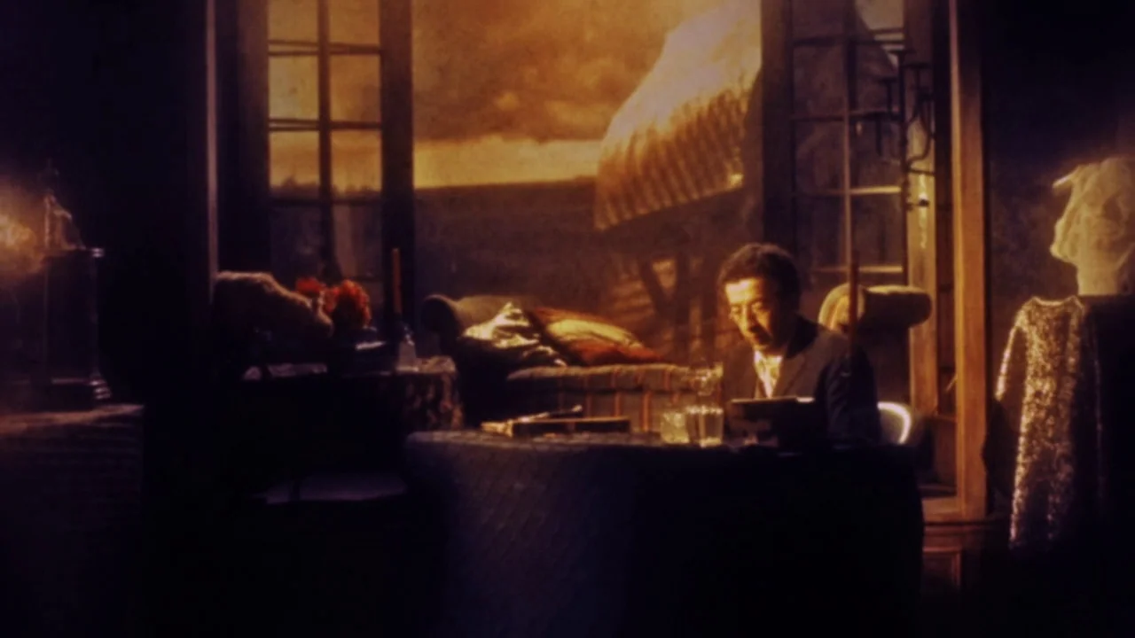 The Forbidden Room (2015) movie still: medium — A dimly lit room features a man sitting at a dark table before a window. Outside the window is a…