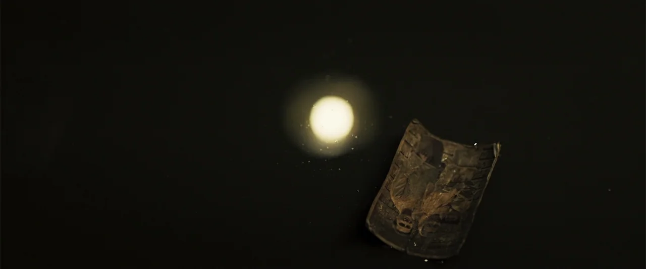 The Unholy (2022) movie still: closeup — A small curved photograph lies on a dark, reflective surface in near darkness. A bright circular light…